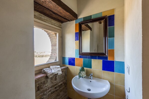 A bathroom with a white sink, a mirror, and a window with a view of a desert landscape.