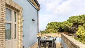 A patio with a table and chairs, a stone wall, and a building with a blue exterior and a stone facade. - LA MASSERIA - La Colombaia - 6 (Vasto)