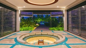 Un vestíbulo espacioso con una zona de estar central, un recinto de cristal con vistas a un jardín tropical y un diseño de techo moderno.