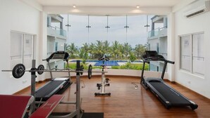 Un gimnasio con cintas de correr, una prensa de banca y una estructura para sentadillas, con grandes ventanales que dan a una piscina y palmeras.