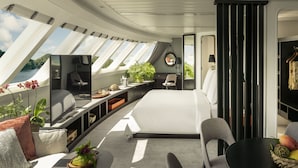 A modern interior with a bed, seating area, and a view of the outdoors. - Four Seasons Explorer, Palau - Cruising Resort (Koror)