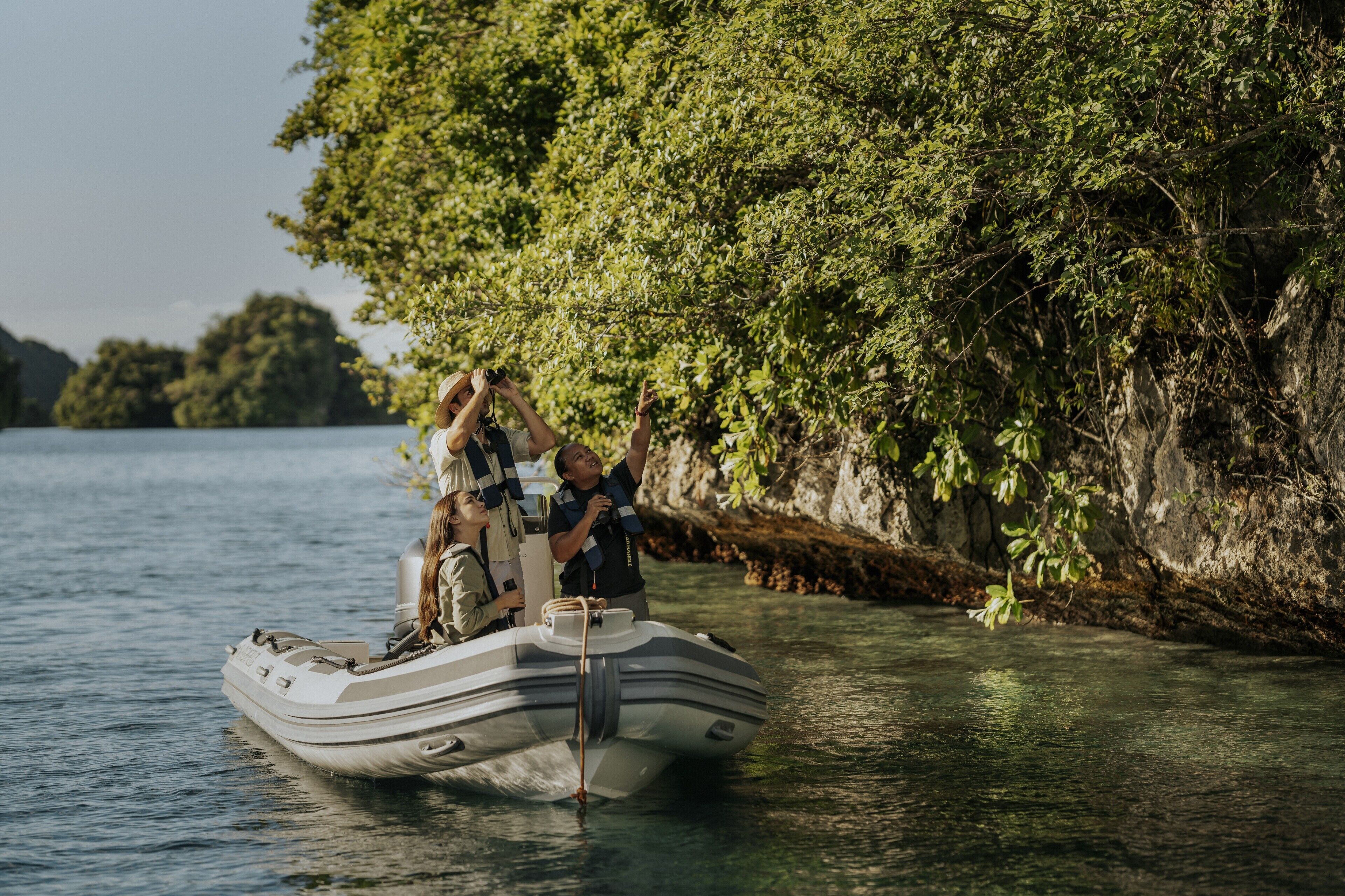 A small inflatable boat on calm water near a rocky shore with dense foliage.