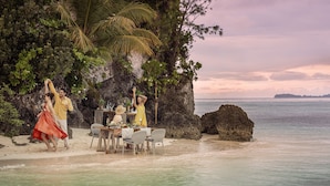 A beachside dining setup with a table and chairs, a rocky backdrop, and a view of the ocean. - Four Seasons Explorer, Palau - Cruising Resort (Koror)