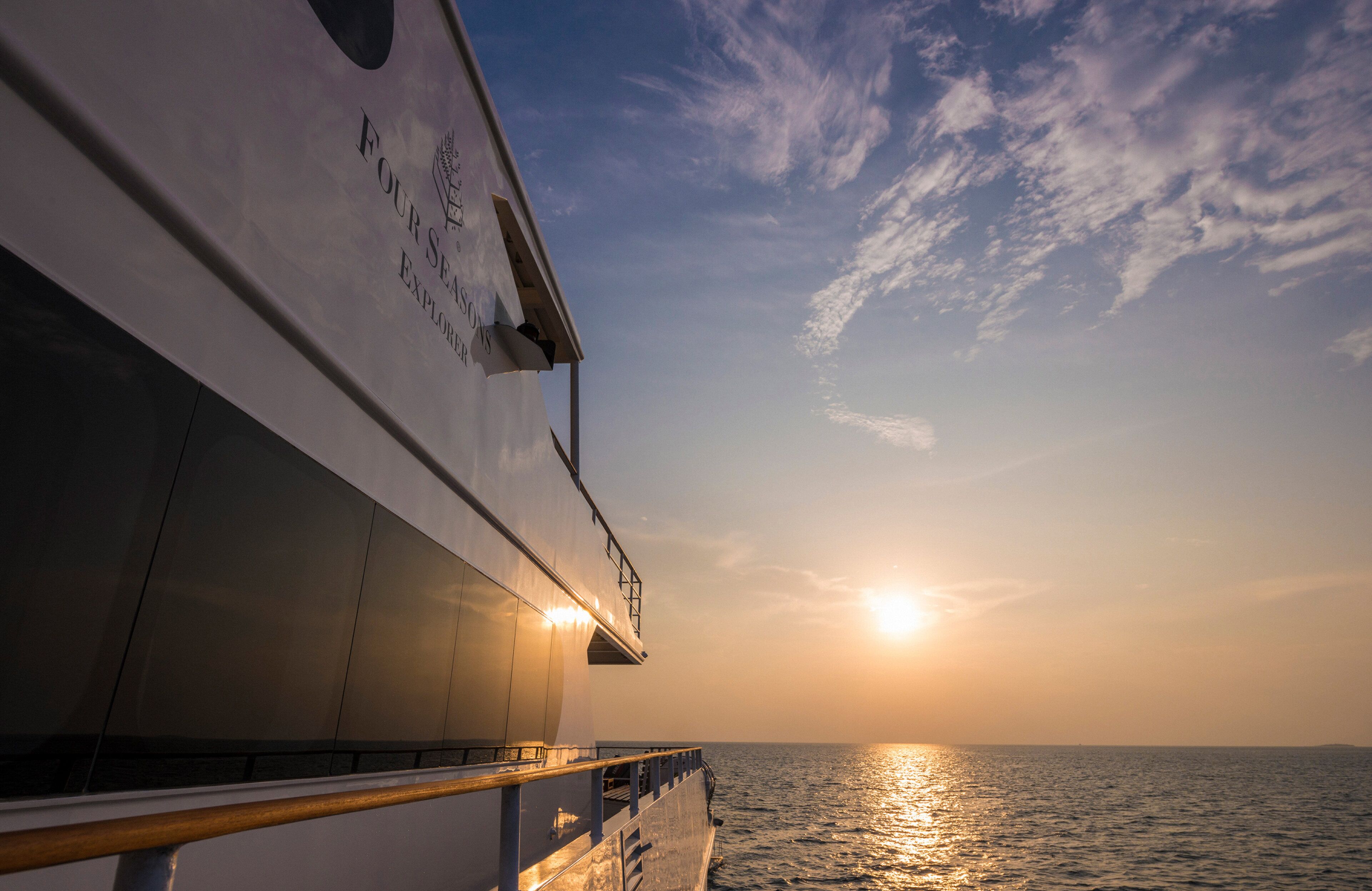 A cruise ship's deck with a sunset view, including the ship's name and a railing.