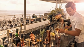 A bar area with a bartender preparing drinks, a variety of bottles, glasses, and a view of the ocean. - Four Seasons Explorer, Palau - Cruising Resort (Koror)