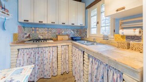 Cocina con armarios blancos, salpicadero de azulejos y ventana con cortinas.