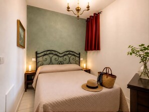 Una camera da letto con un letto, abat-jour, un quadro appeso al muro, una tenda rossa, un cesto di vimini e un vaso con una pianta.