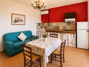 Cocina compacta con pared roja, refrigerador blanco y comedor con mesa y sillas.