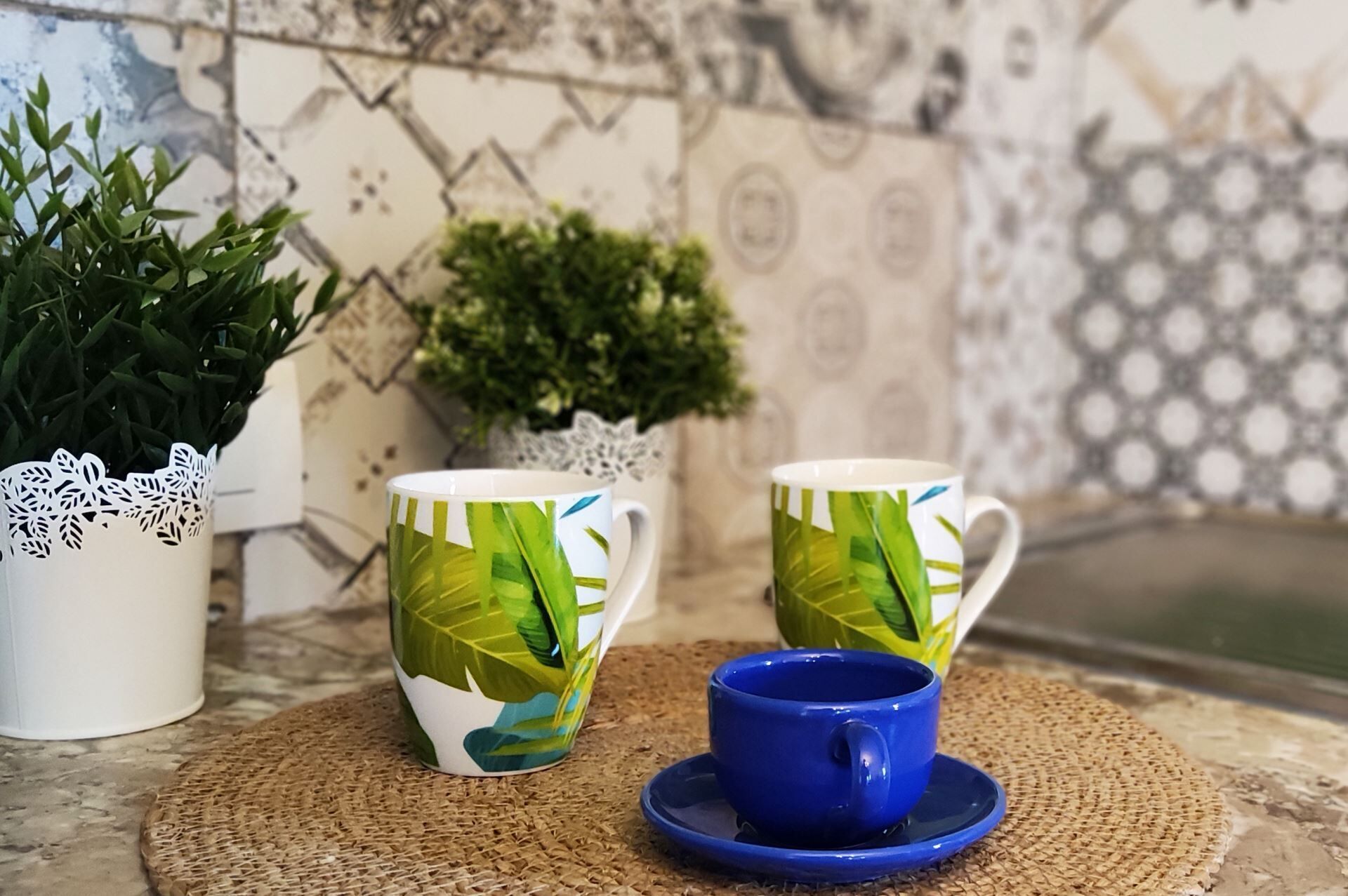 Zwei grüne und weiße Tassen mit Muster, eine blaue Tasse und ein weißer dekorativer Gegenstand mit spitzenartigen Mustern.