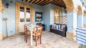 Eine überdachte Terrasse mit Esstisch, Korbmöbeln und einer Ziegelwand.