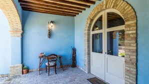 A covered patio area with a brick floor, a wooden table with chairs, a potted cactus, and a white door with a window. - LA MASSERIA - La Rimessa - 9 (Vasto)