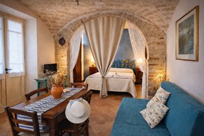 A cozy room with a bed, a blue sofa, a dining table with chairs, and a large window.