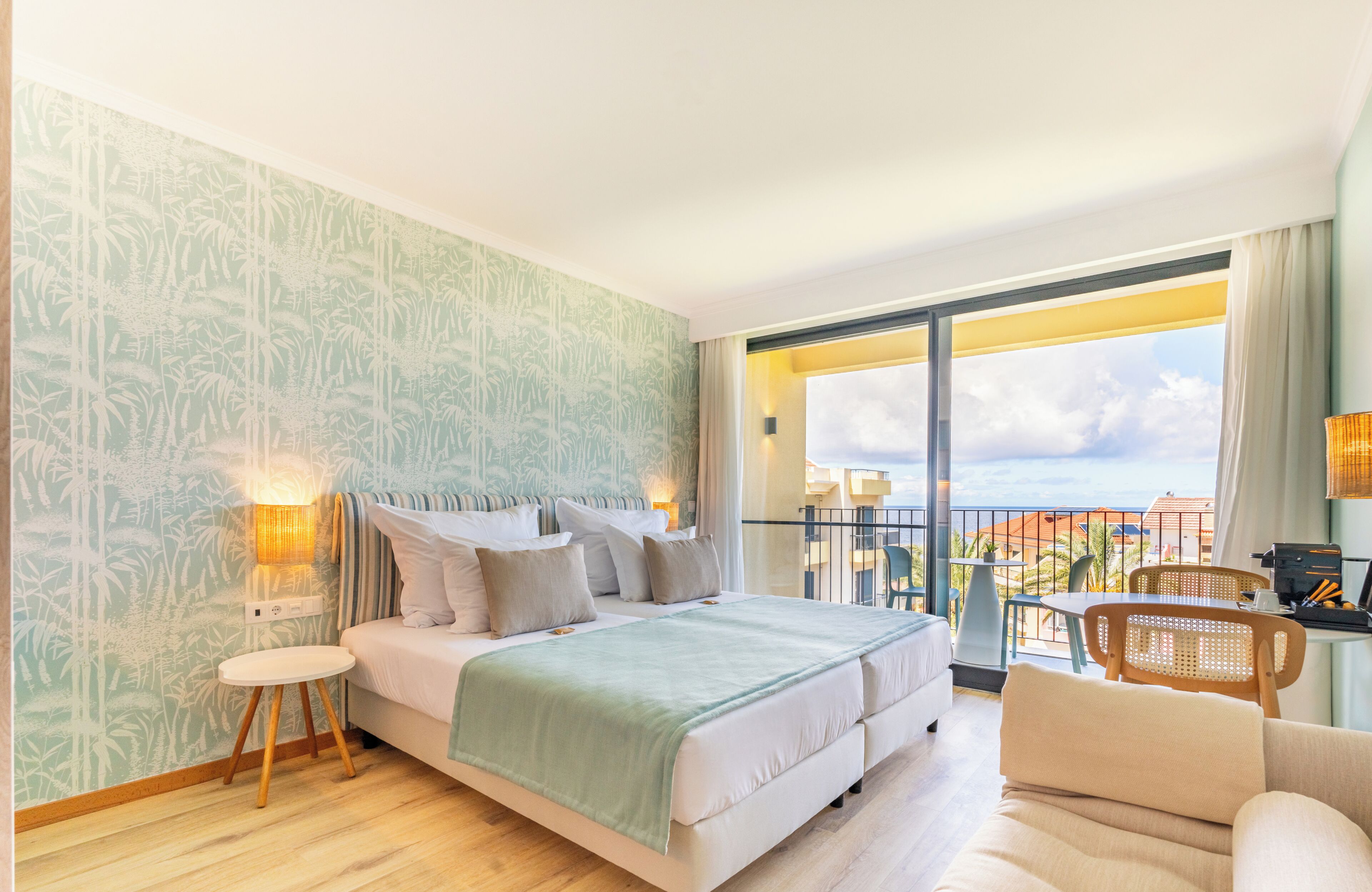 Een slaapkamer met een bed, een klein rond tafeltje, een stoel en een balkon met uitzicht.