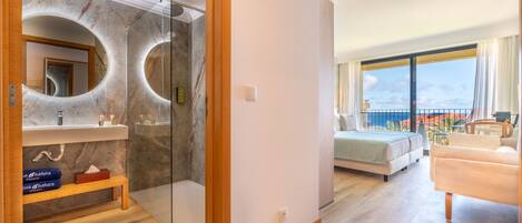 Quarto de hotel moderno com banheiro de mármore, varanda com cama e vista para o mar.