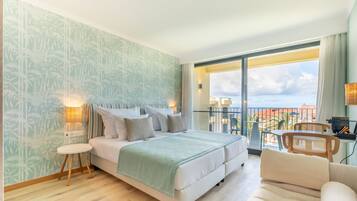 A modern bedroom with a large bed, a small round table, a sofa, and a balcony with a view of the city.