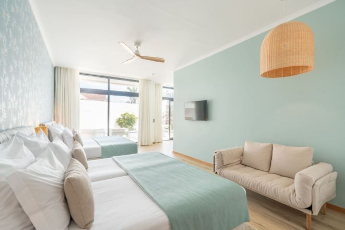 A modern hotel room with a bed, a sofa, a TV, and a ceiling fan.