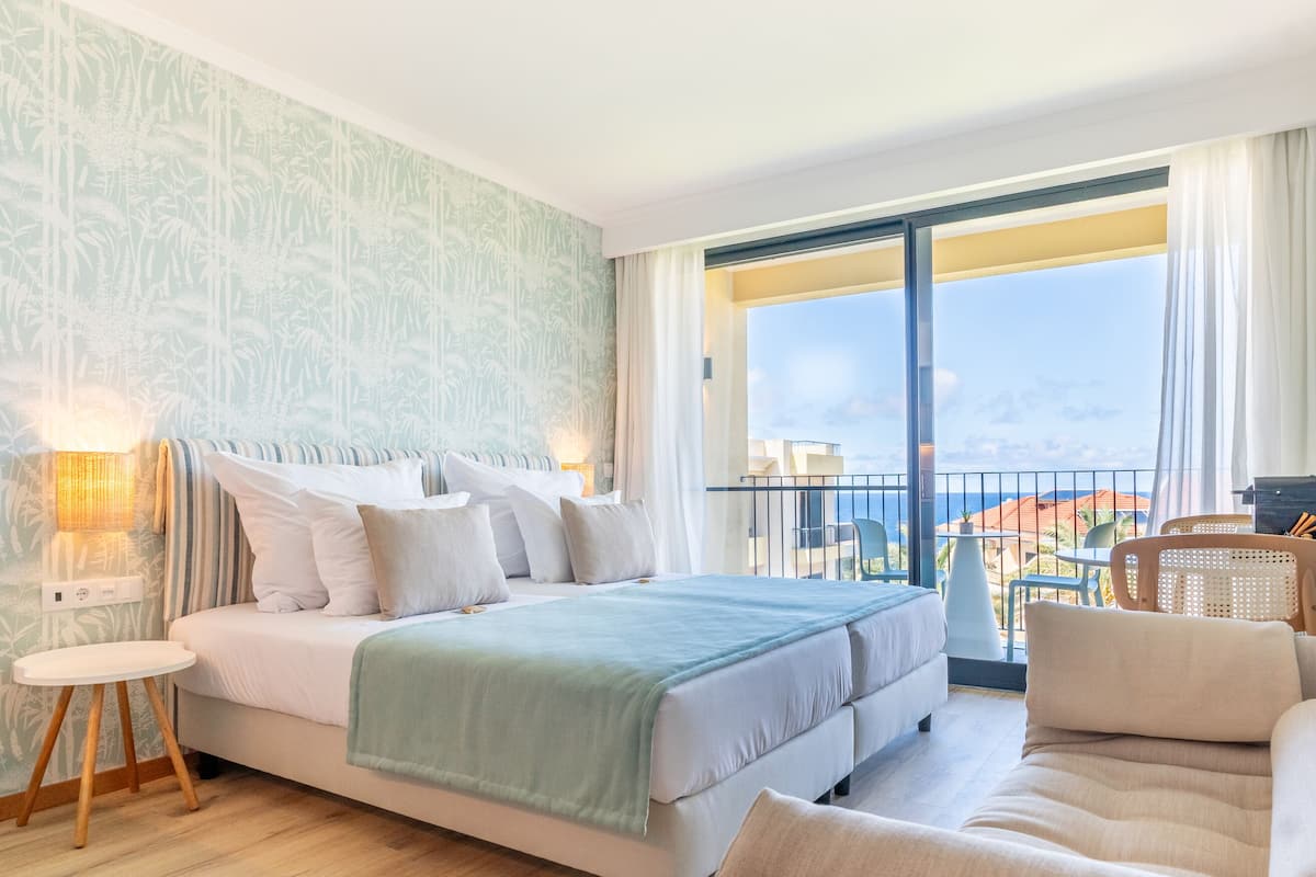 A hotel room with a large bed, a sofa, a small table, and a balcony with a view.