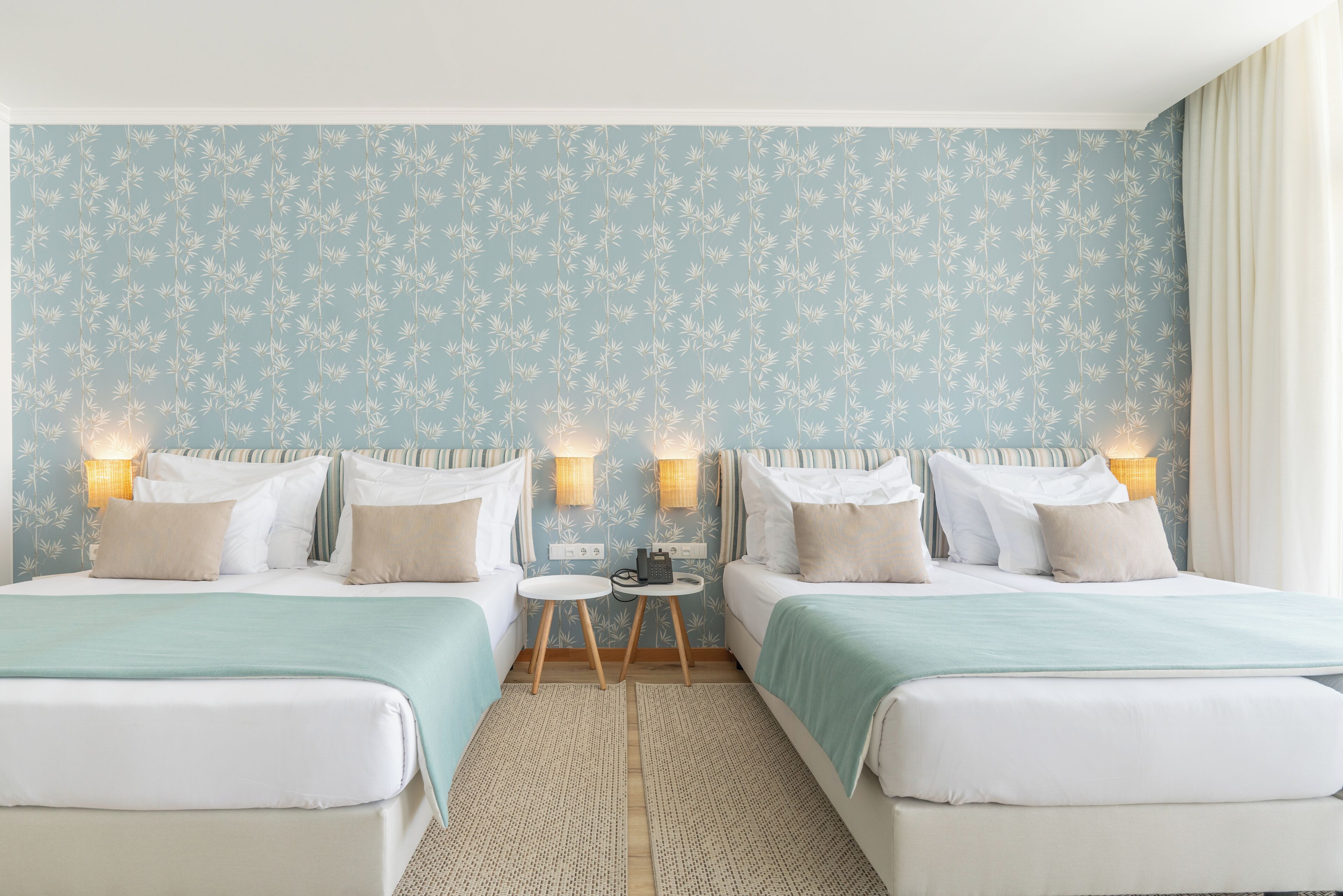 A hotel room with two beds, a small table, and two wall-mounted lamps.