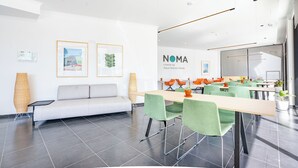 A modern conference room with a long table, green chairs, and a white sofa. There are framed pictures on the wall and a sign that reads "NOMA cowork by Aqua Natura Hotels." - Studios by Aqua Natura Hotels (Porto Moniz)