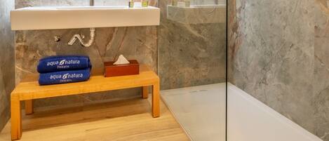 Un baño moderno con pared de mármol, un banco de madera y cabina de ducha de vidrio.