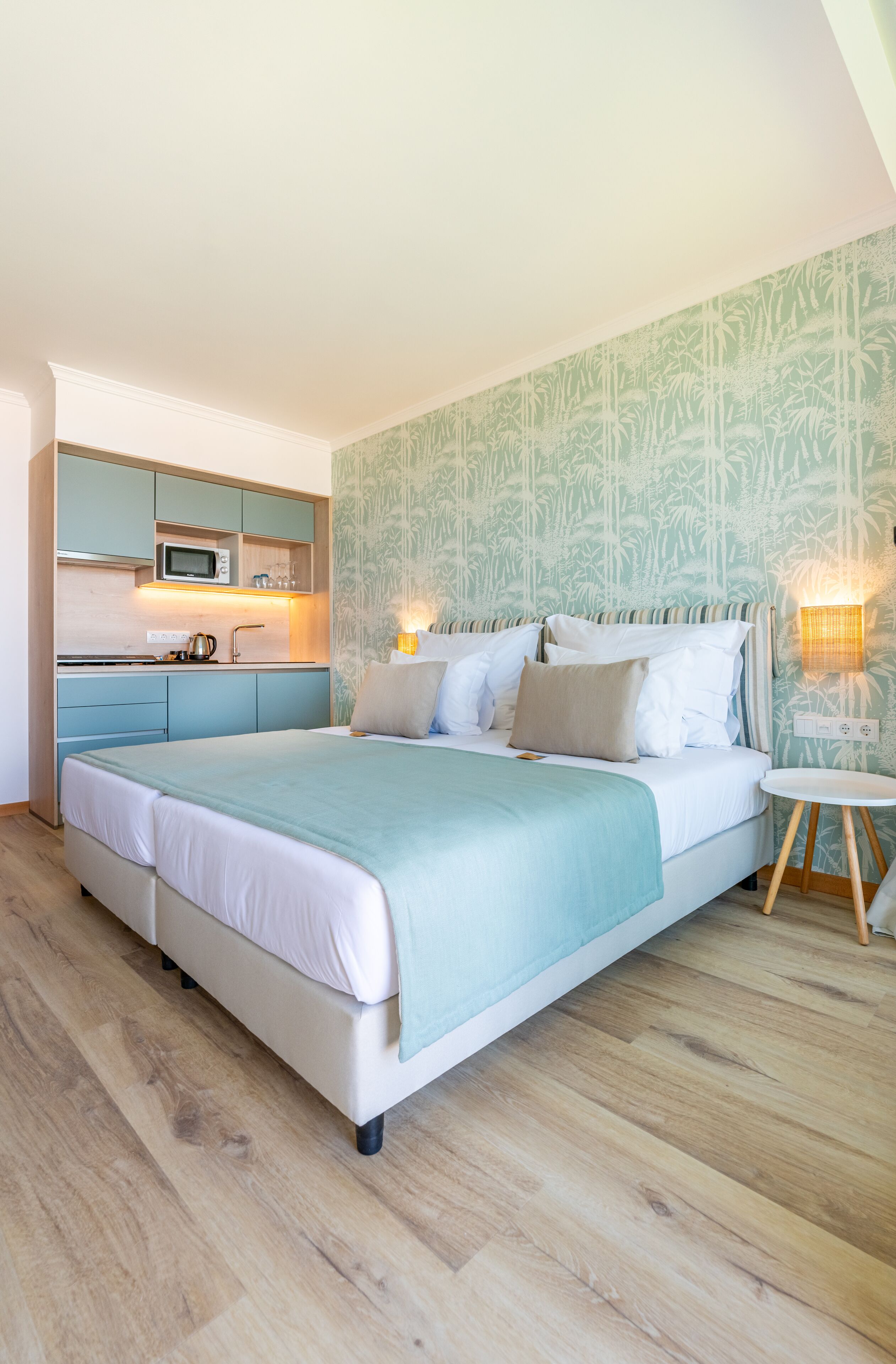 A bedroom with a bed, bedside table, and a kitchenette area with a microwave.
