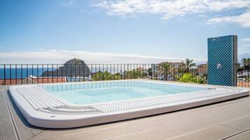 A rectangular hot tub on a deck with a view of the sea and a mountain in the background.