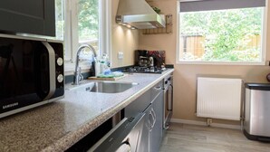 A modern kitchen with a built-in microwave, stainless steel appliances, a double sink, and a window with a view of greenery. - Cosy cottage at Veluwe (Putten)