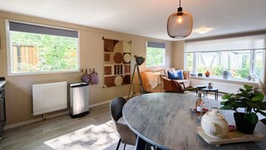 A modern kitchen with a large dining table, a hanging light fixture, and a view of the outdoors. - Cosy cottage at Veluwe (Putten)