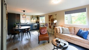 A modern kitchen with dark cabinetry, a dining area with a round table and chairs, a leather armchair, and a beige sofa with cushions. - Cosy cottage at Veluwe (Putten)