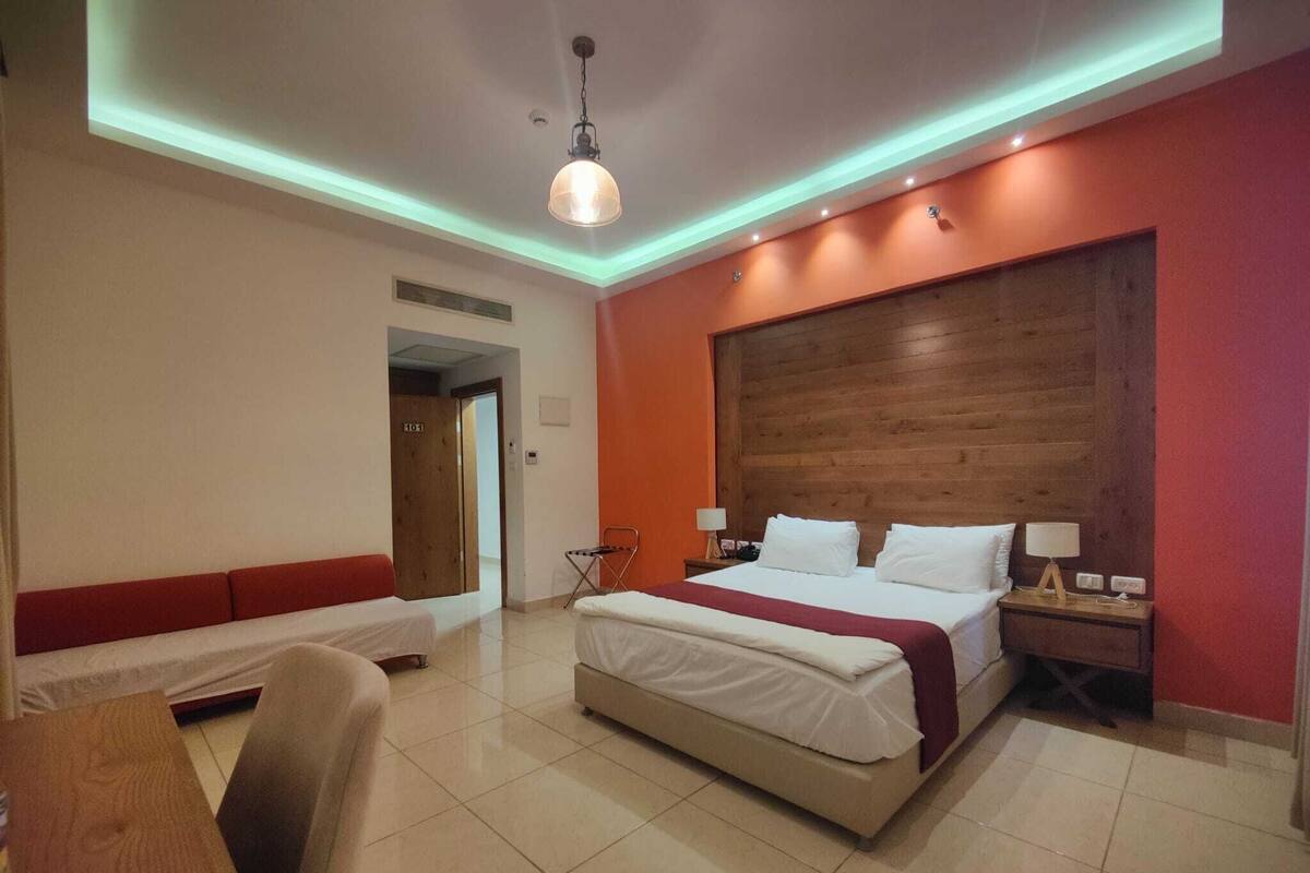Ein Hotelzimmer mit einem großen Bett, einer Bank, einem Schreibtisch und einem Holz-Kopfteil.