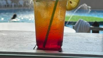 A glass of iced drink with a lemon slice and mint on a table near a pool.