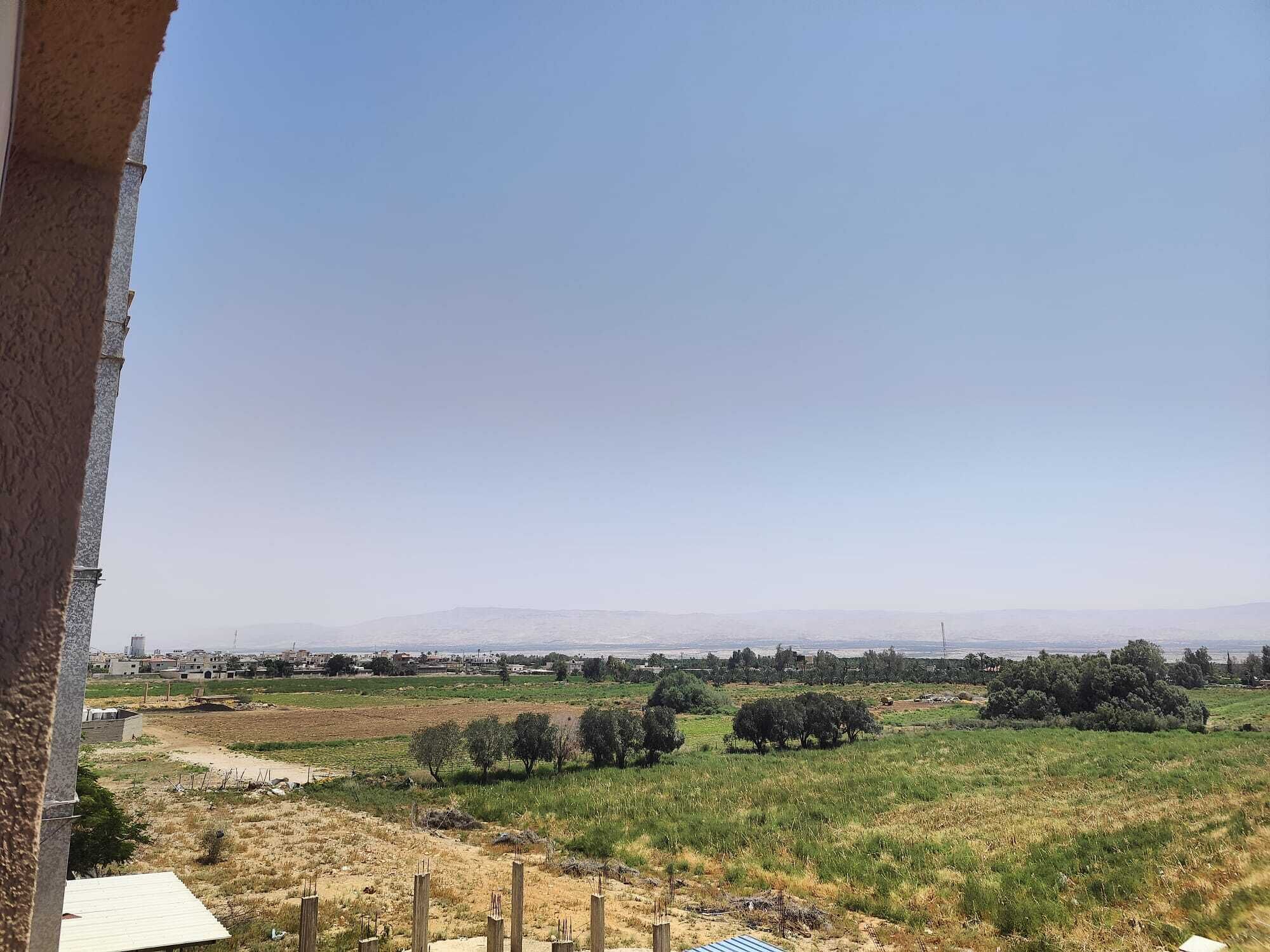 A view from a balcony overlooking a rural landscape with fields, trees, and distant buildings.