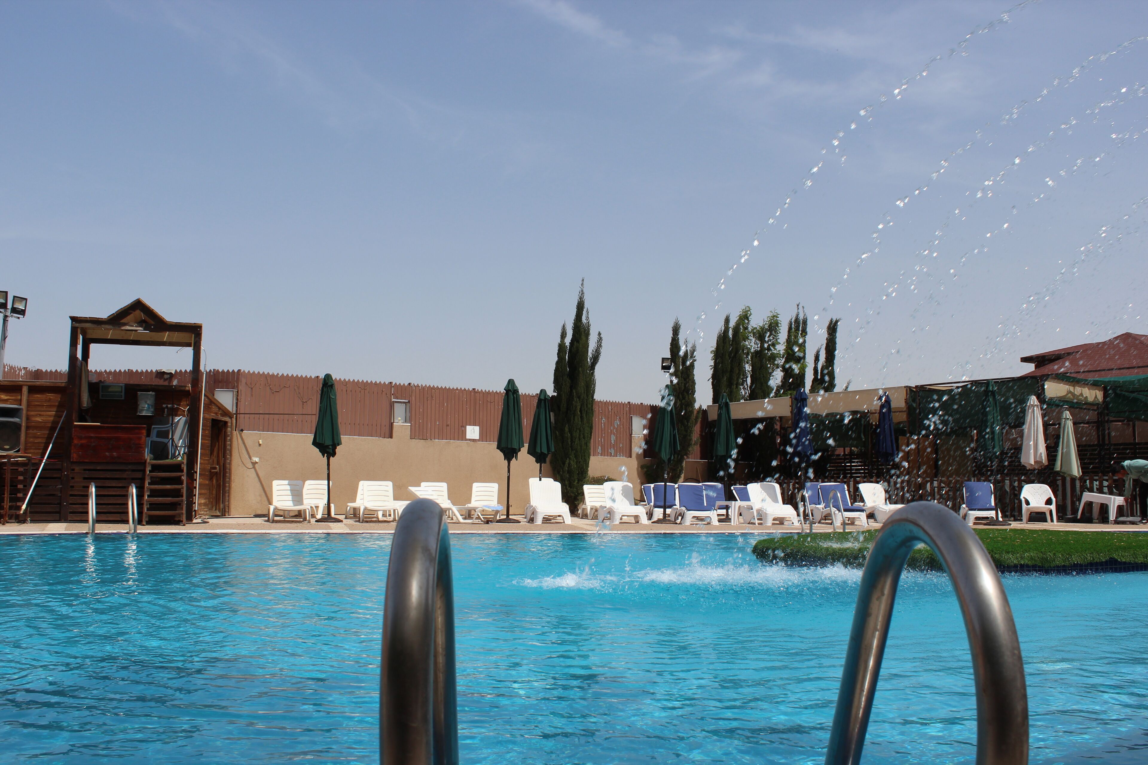 A swimming pool with lounge chairs and umbrellas, a wooden structure, and tall trees in the background.