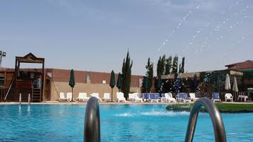 A swimming pool with lounge chairs and umbrellas, a wooden structure, and tall trees in the background.