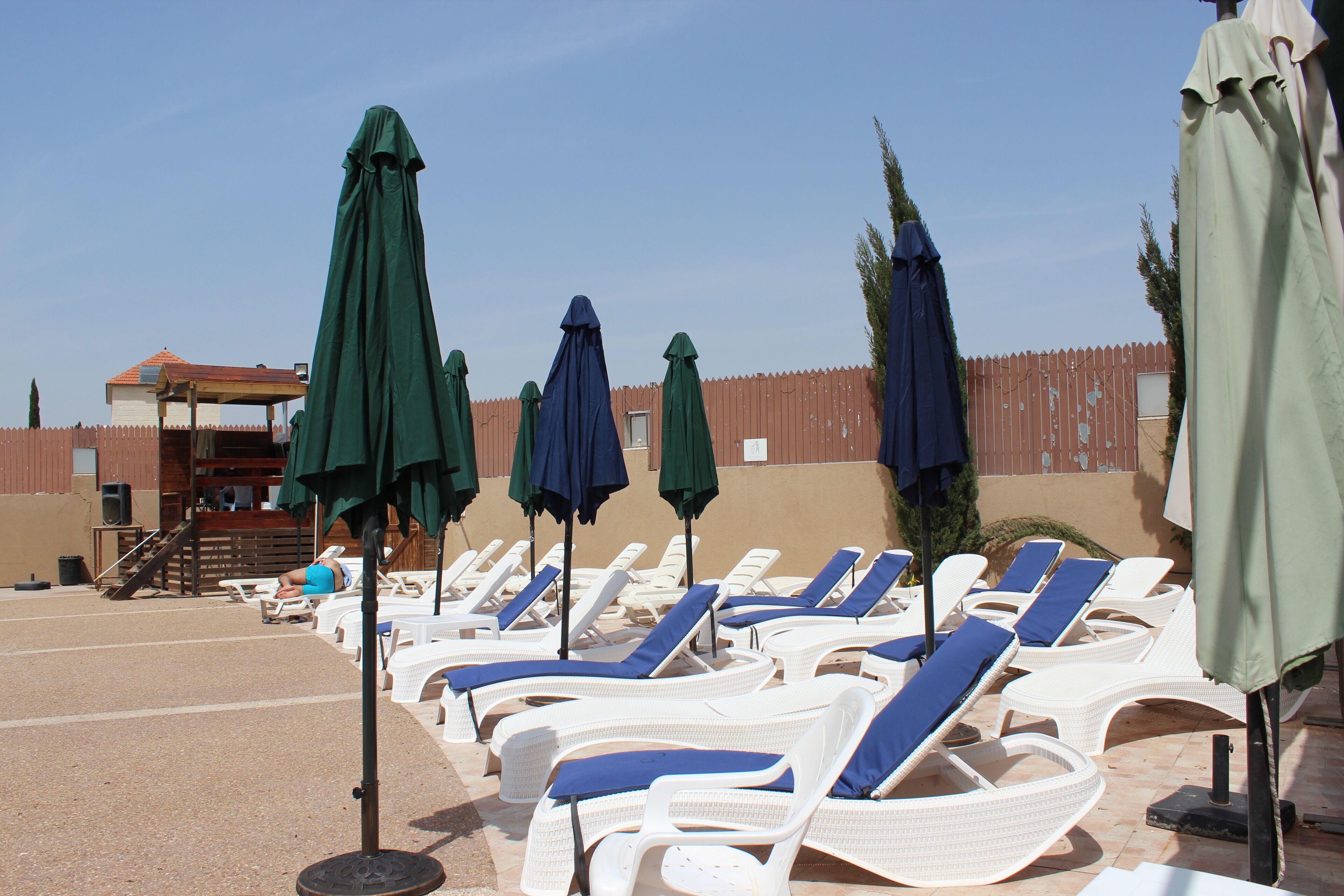A poolside area with white lounge chairs and green umbrellas.