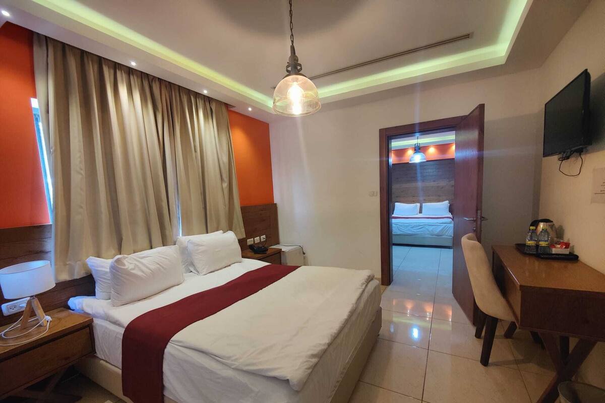 Ein Hotelzimmer mit Bett, Nachttisch, Lampe, Schreibtisch, Stuhl und Fernseher an der Wand.