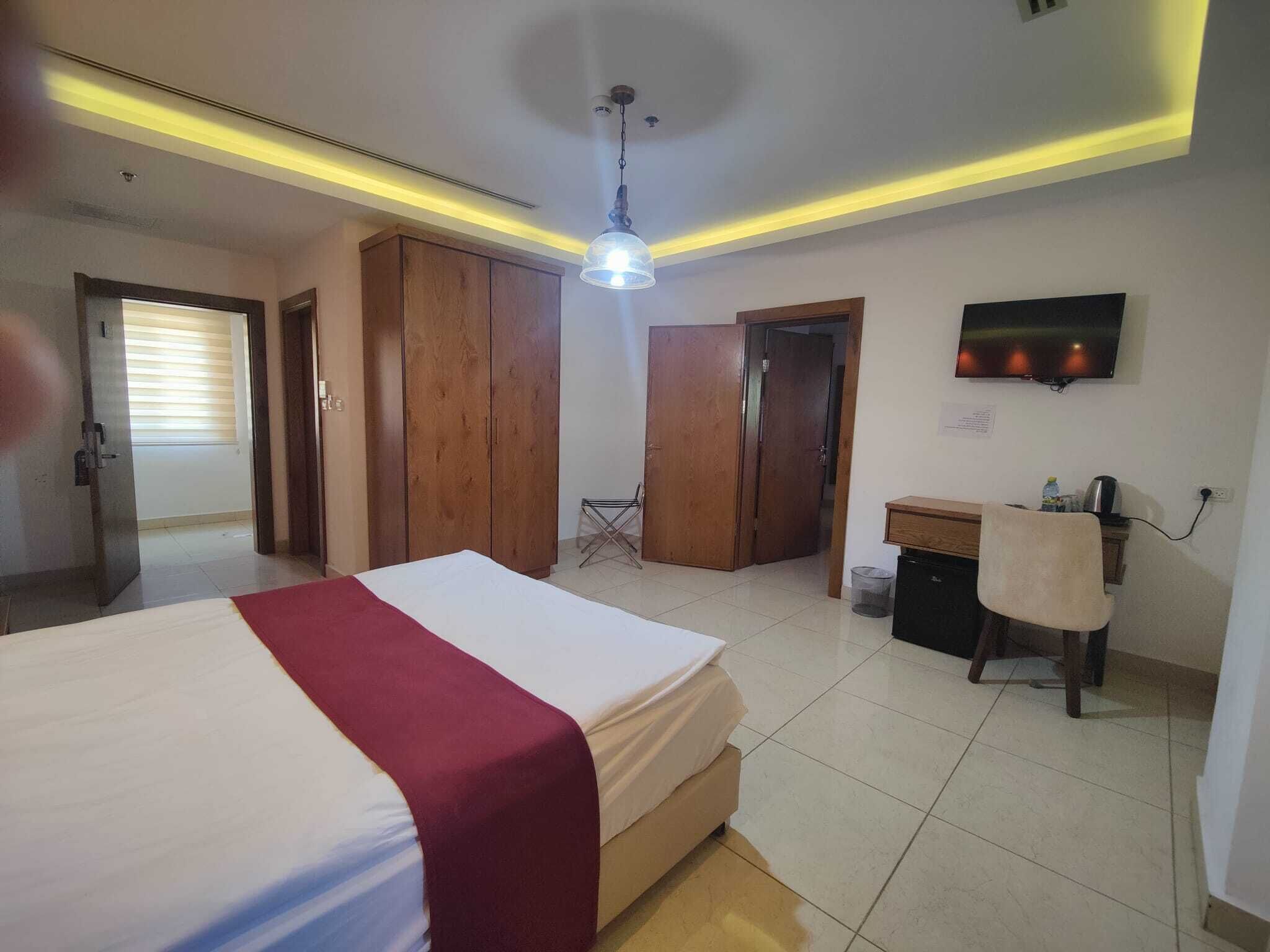 Habitación de hotel con cama, escritorio, silla, televisor y armario.