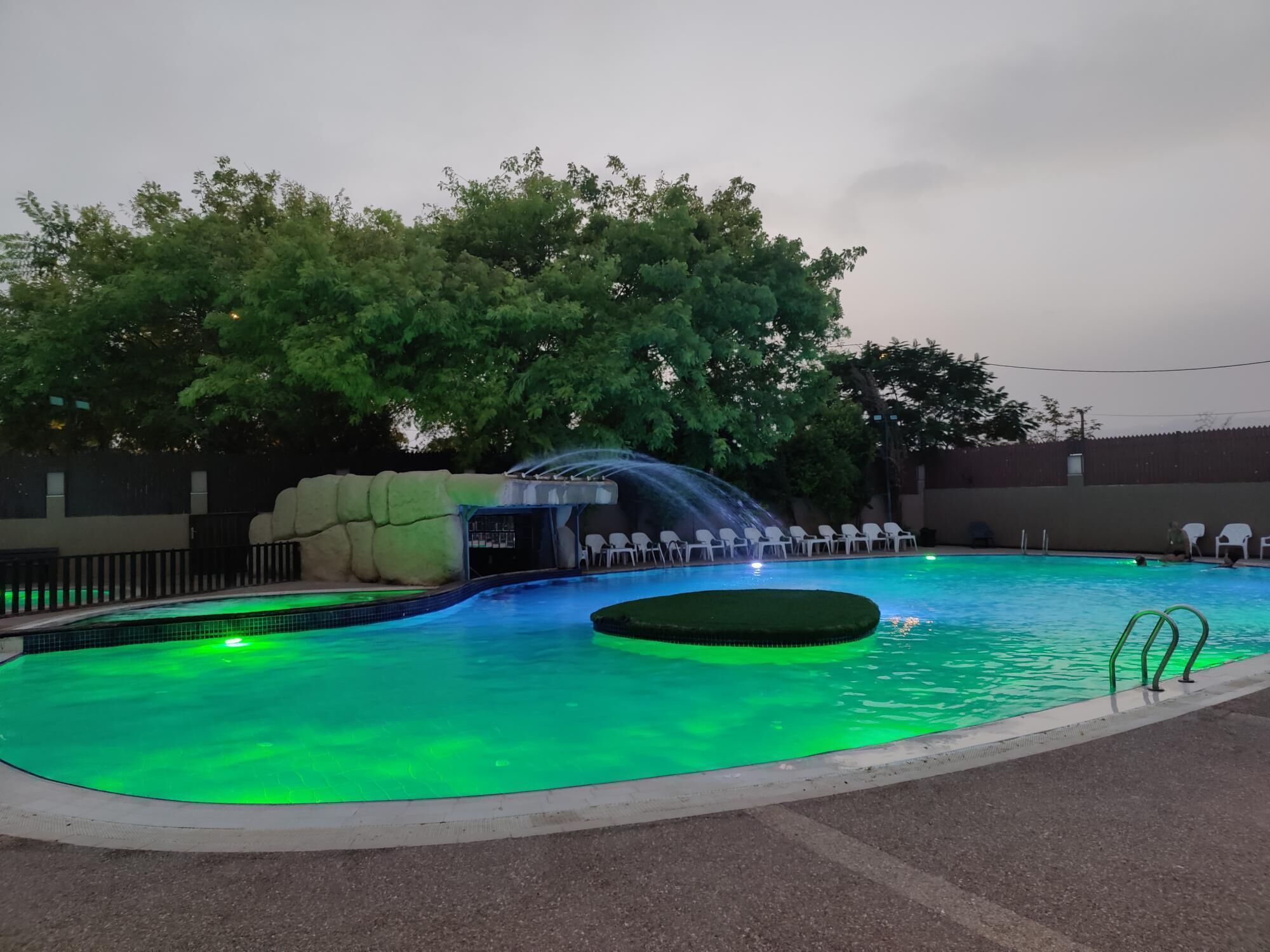 A swimming pool with a waterfall feature, surrounded by trees and a covered seating area.