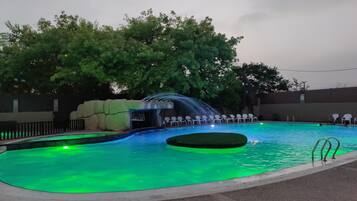 A swimming pool with a waterfall feature, surrounded by trees and a covered seating area.
