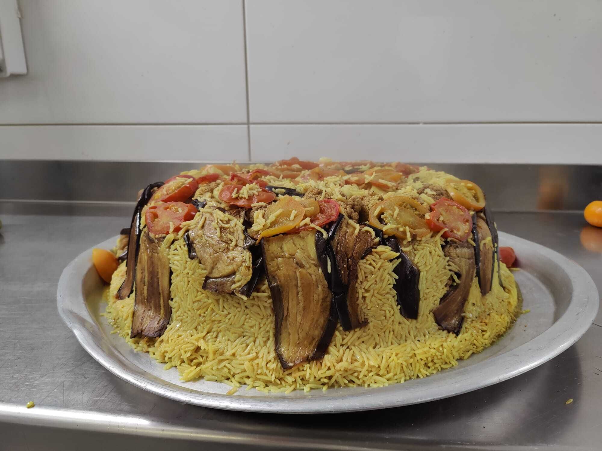 A large, round, yellow rice dish with meat and vegetables on a metal plate.