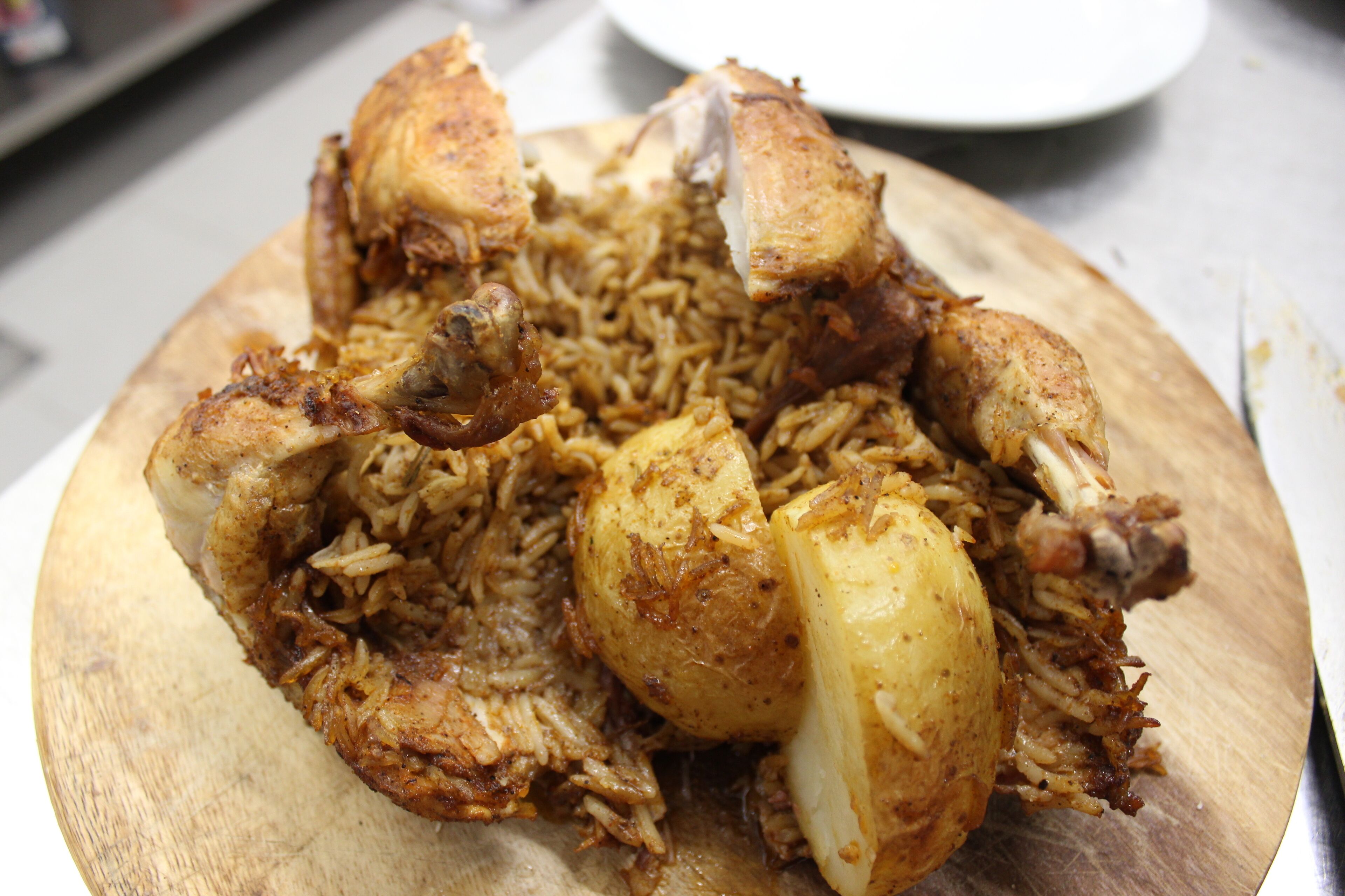 A wooden serving board with a dish of rice and chicken pieces.