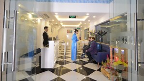 A reception area with a check-in counter, a waiting area with a sofa and chairs, and a decorative plant arrangement. - Hanoi Prime Center Hotel & Spa (Hanoi)