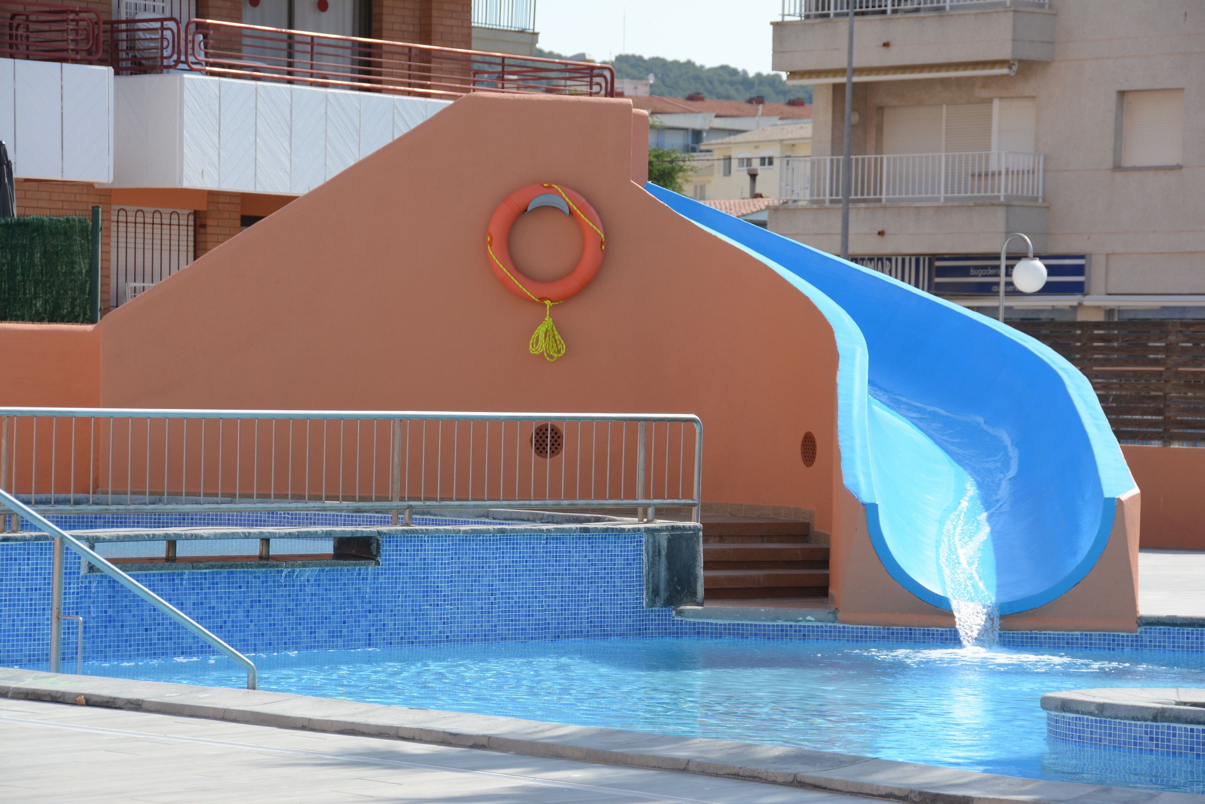 A swimming pool with a blue slide, a lifebuoy, and a metal railing.