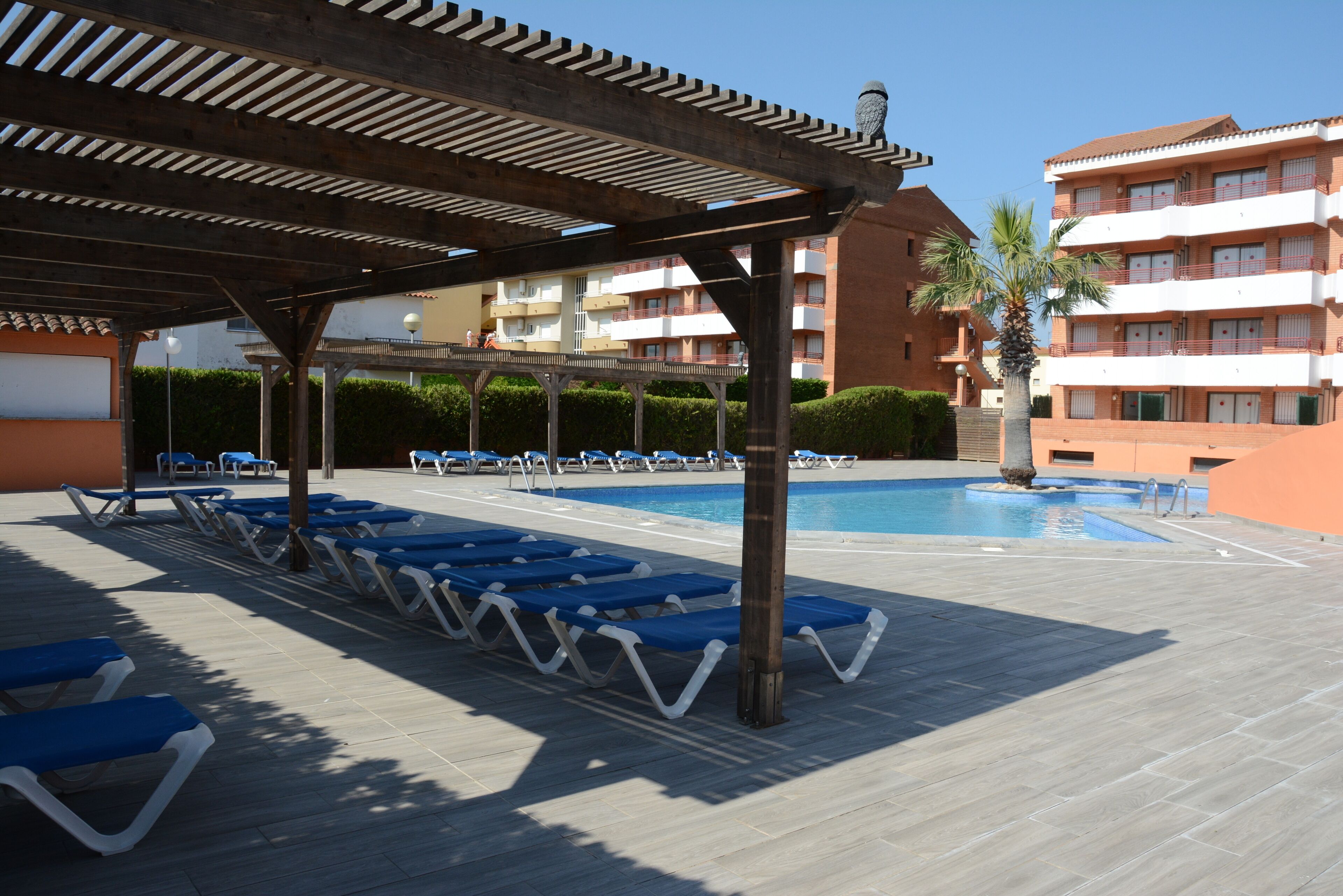 Un área junto a la piscina con sillones de descanso y una pérgola.
