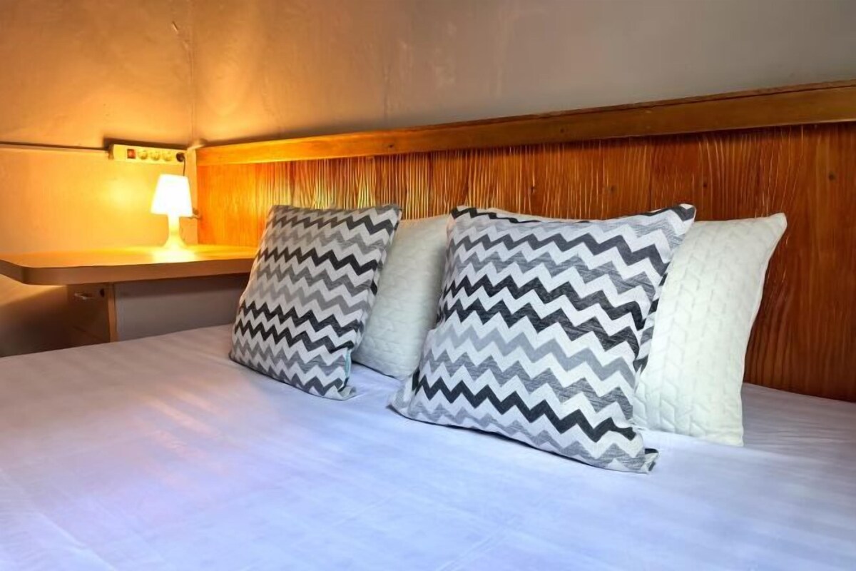 A hotel room with a bed, two pillows with a zigzag pattern, a wooden headboard, and a bedside lamp.