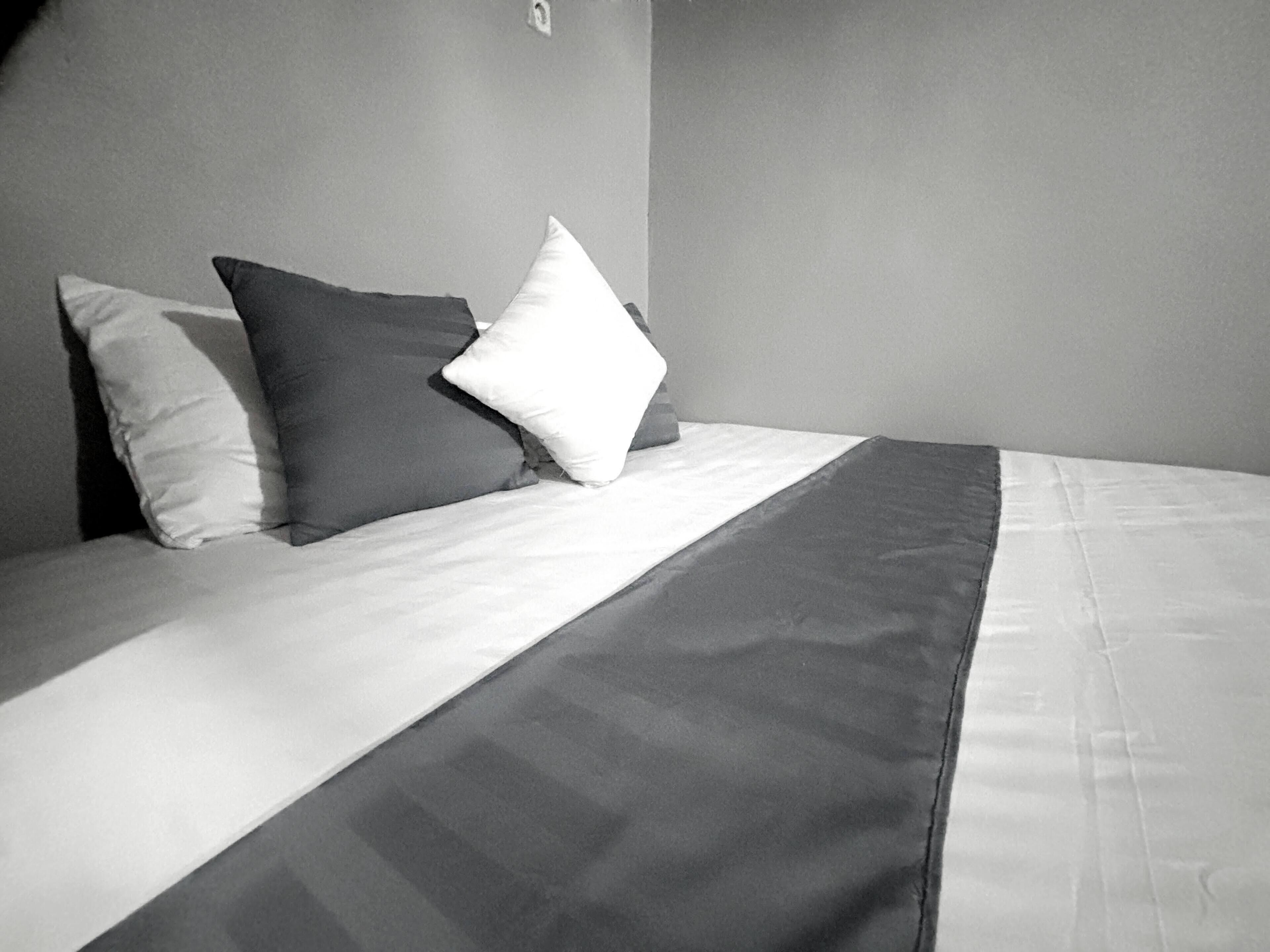 A bed with a white and dark gray blanket, two pillows, and a plain wall.