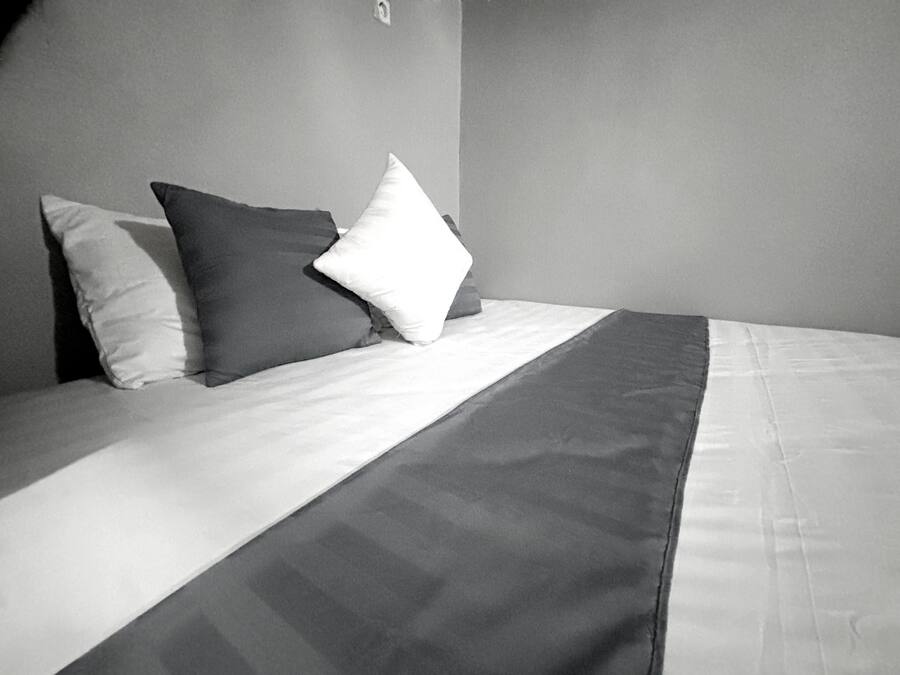 A bed with a white and dark gray blanket, two pillows, and a plain wall.