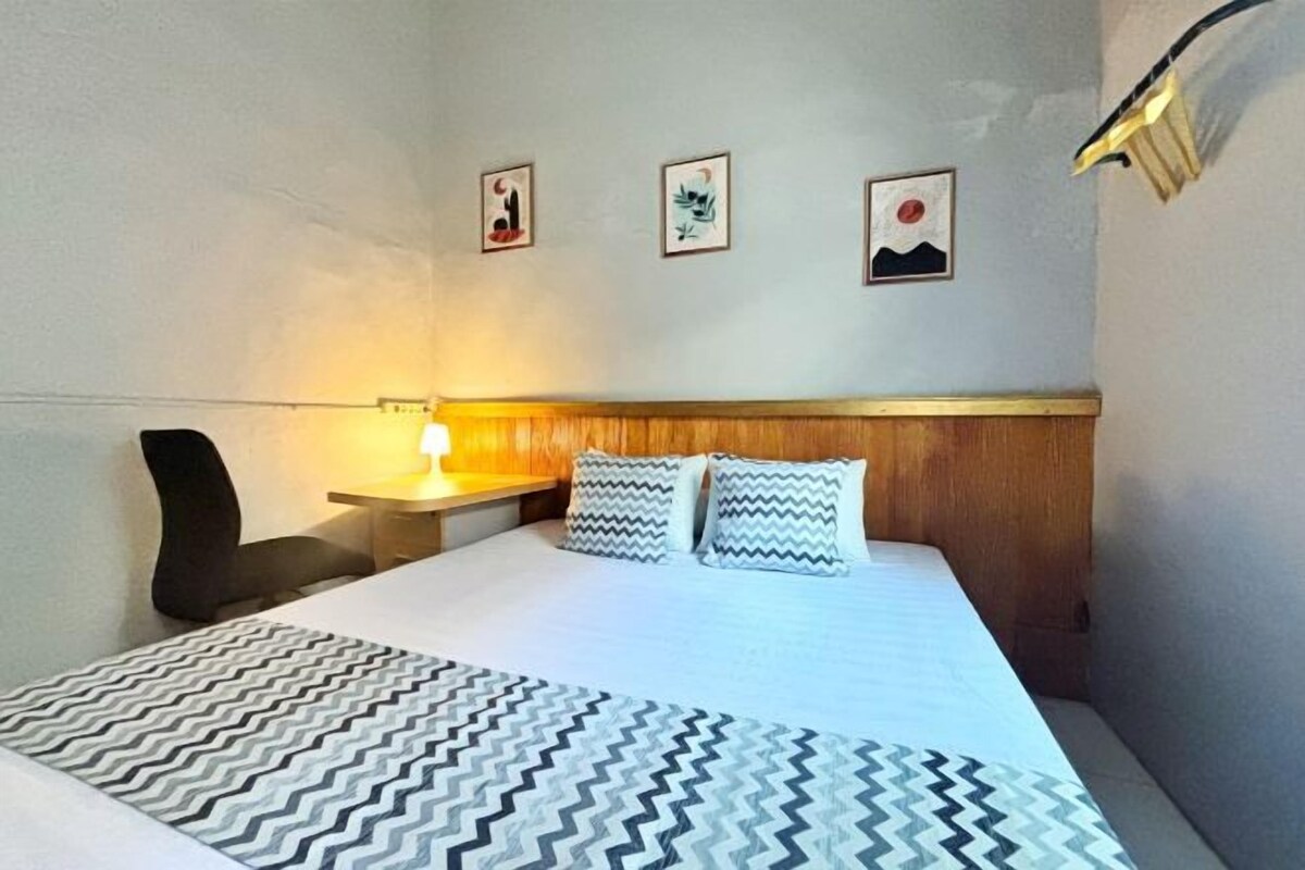 A hotel room with a bed, a nightstand, a chair, and three framed pictures on the wall.
