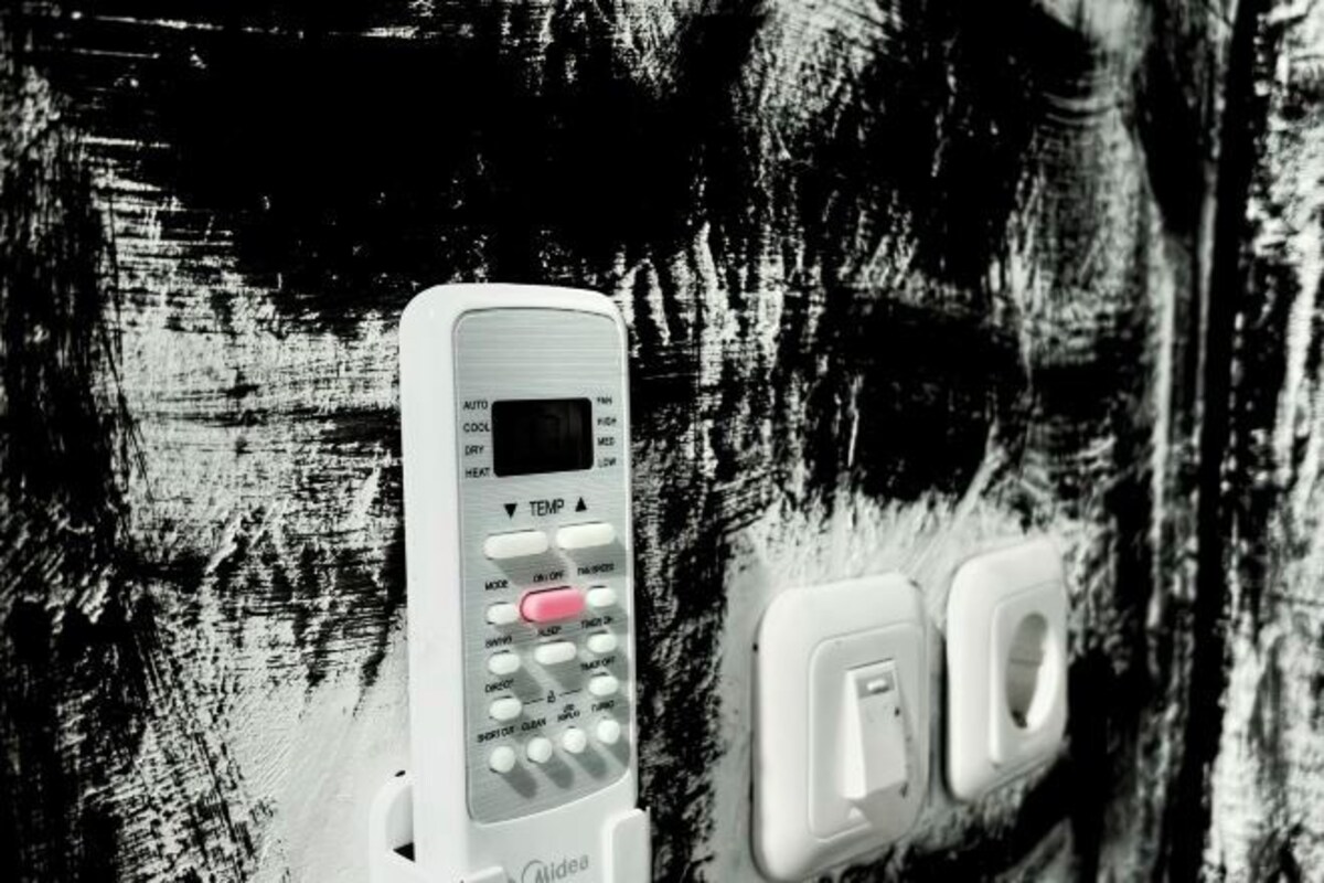 A white thermostat with a digital display and control buttons, mounted on a wall with a textured surface.