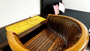 A room with a wooden chair, a small table with a yellow mat, a black cushioned sofa, and a mirror on the wall. - Kost Harian Semarang Murah (Semarang)